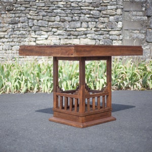 Peut inclure: Une table en bois brun foncé avec un plateau carré et un piétement géométrique ouvert unique. La table est en bois massif et a un aspect rustique et artisanal.