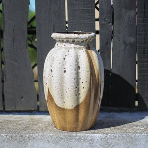 Può includere: Un vaso in ceramica bianco e marrone con una glassa macchiettata. Il vaso ha una forma arrotondata e bulbosa con un collo stretto.