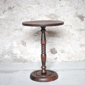 Pode incluir: Uma mesa de pedestal de madeira castanho-escura com um tampo circular, uma coluna central torneada com detalhes canelados decorativos e uma base redonda resistente. O veio da madeira &eacute; vis&iacute;vel, apresentando um acabamento liso e polido.