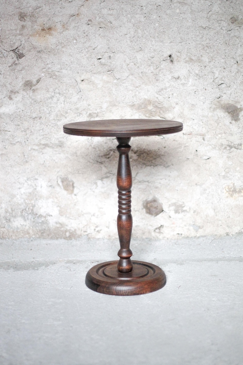 Pode incluir: Uma mesa de pedestal de madeira castanho-escura com um tampo circular, uma coluna central torneada com detalhes canelados decorativos e uma base redonda resistente. O veio da madeira &eacute; vis&iacute;vel, apresentando um acabamento liso e polido.