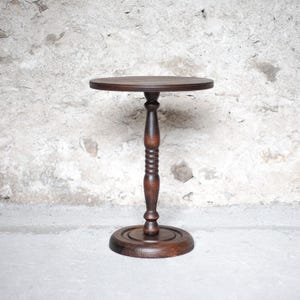 Pode incluir: Uma mesa de pedestal de madeira castanho-escura com um tampo circular, uma coluna central com um design torneado e canelado, e uma base redonda e plana. A mesa &eacute; constru&iacute;da em madeira com veios vis&iacute;veis e um acabamento polido e liso.