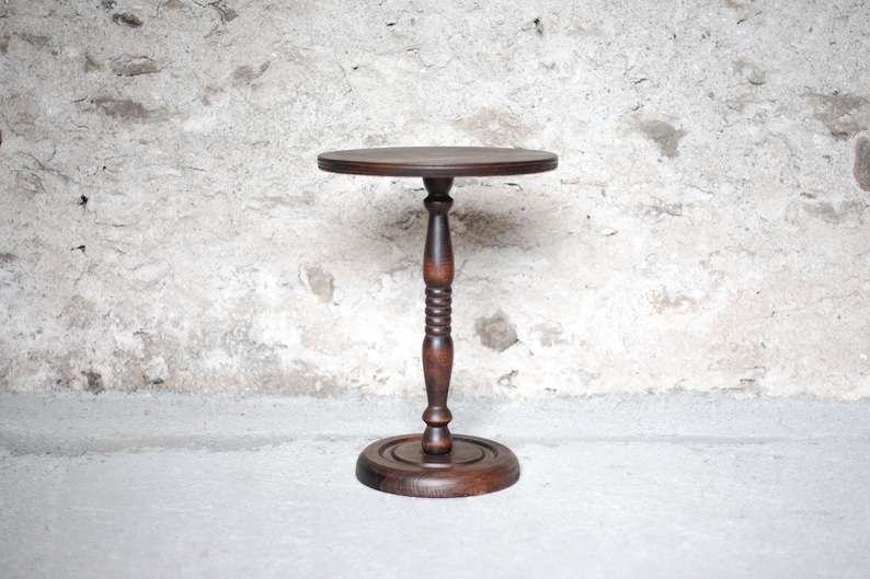 Pode incluir: Uma mesa de pedestal de madeira castanho-escura com um tampo circular, uma coluna central com um design torneado e canelado, e uma base redonda e plana. A mesa &eacute; constru&iacute;da em madeira com veios vis&iacute;veis e um acabamento polido e liso.