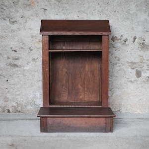 Peut inclure: Un prie-dieu en bois brun foncé doté d'une tablette supérieure inclinée pour poser des livres ou des objets, d'un panneau arrière vertical et d'une plateforme de base horizontale pour s'agenouiller, avec un grain de bois visible.