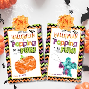 May include: Two Halloween-themed gift bags with orange and green zig-zag borders. Each bag features a colorful pop-it toy and the text "Hope Your Halloween is Popping with Fun!" One bag has a pumpkin pop-it, the other a ghost.