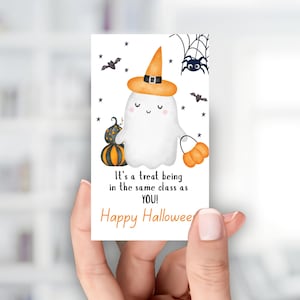 Puede incluir: Una etiqueta de regalo de Halloween con un fantasma de dibujos animados que lleva un sombrero de bruja y una bolsa de golosinas con forma de calabaza. La etiqueta incluye el texto "It's a treat being in the same class as YOU!" y "Happy Halloween."