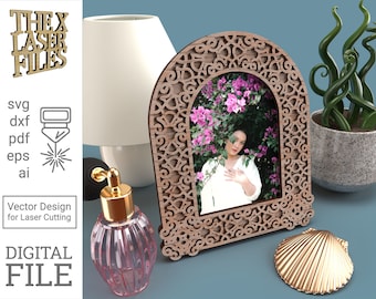 May include: A wooden picture frame with a decorative, intricate design. The frame is arched at the top and has a cutout design that resembles a window. The frame is sitting on a table with a seashell and a bottle of perfume.