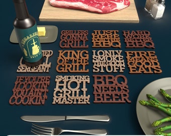 May include: A set of nine wooden coasters with different sayings related to grilling and BBQ. The coasters feature phrases like "Grillers Gonna Grill", "King of the Grill", "Smoking Hot Grill Master", and "BBQ Needs Beer".