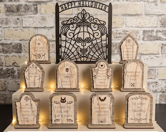 May include: A collection of ten wooden tombstone-shaped signs with engraved humorous text and a large black laser-cut arch featuring a skull and spiderweb design. The text includes phrases like Finally, Death by Dad Jokes, and I'd rather be haunting you.