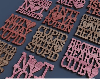 May include: A set of 10 laser cut wood designs with Valentine's Day themed sayings. The designs are in shades of brown and pink with a broken heart graphic on each. The sayings include "Cupid Rhymes with Stupid", "Not Today Cupid", "Anti Love Potion", "Chasing Dreams Not Hearts", "Broken Hearts Club", "Cheer Up One Heart", "Cupid's Arrow Missed Me", "Love is True", and "Not You It's Me".