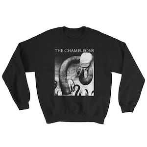 May include: Black sweatshirt featuring a white graphic of a creature with a long neck and a head resembling a human face. The text "THE CHAMELEONS" is printed above the graphic.