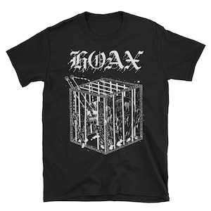 Puede incluir: Camiseta negra con un gráfico blanco de una jaula con una persona dentro y la palabra "HOAX" en una fuente gótica encima. El diseño es una ilustración detallada.