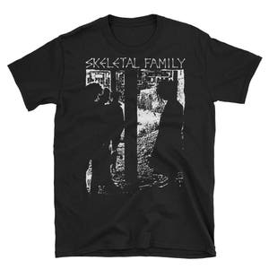 May include: Black t-shirt with a white graphic print of two figures standing in front of a building. The text "SKELETAL FAMILY" is printed above the figures.