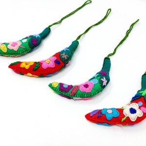 May include: Four handmade green and red felt chili pepper ornaments with colourful embroidered flowers. Each ornament has a green string for hanging.