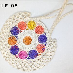 Pu&ograve; includere: Una borsa rotonda intrecciata color bianco sporco con l'etichetta STYLE 05, caratterizzata da un motivo circolare centrale di vivaci rosette floreali multicolori nei toni dell'arancione, giallo, viola e rosa, con due manici intrecciati abbinati.