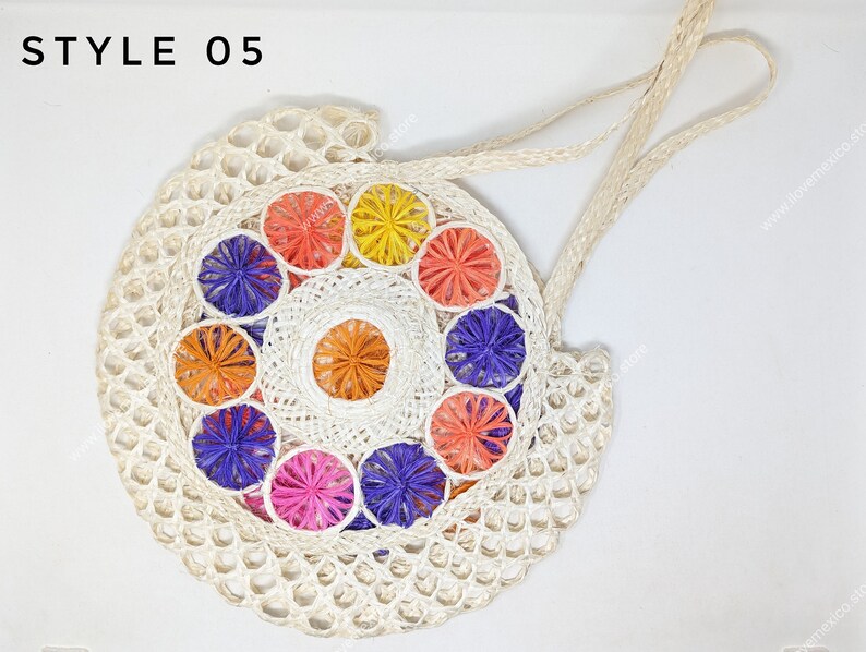 Pu&ograve; includere: Una borsa rotonda intrecciata color bianco sporco con l'etichetta STYLE 05, caratterizzata da un motivo circolare centrale di vivaci rosette floreali multicolori nei toni dell'arancione, giallo, viola e rosa, con due manici intrecciati abbinati.