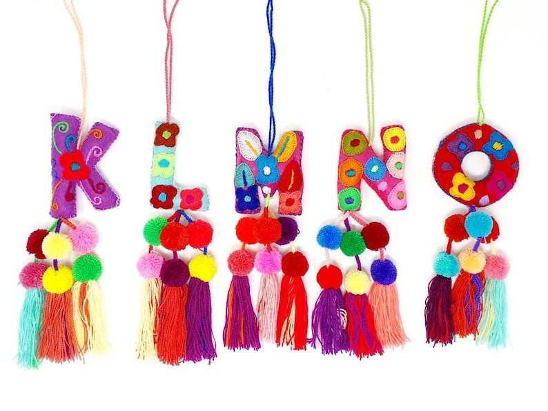 May include: Five colourful felt letter ornaments with pom-pom tassels. The letters are K, L, M, N, and O. Each letter is embroidered with colourful flowers and has a pink, purple, red, or green tassel.