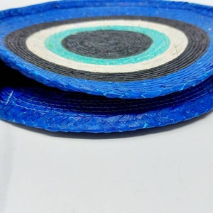 May include: A round, blue and white woven bag with a white woven strap. The bag has a circular pattern of blue, white, and black.