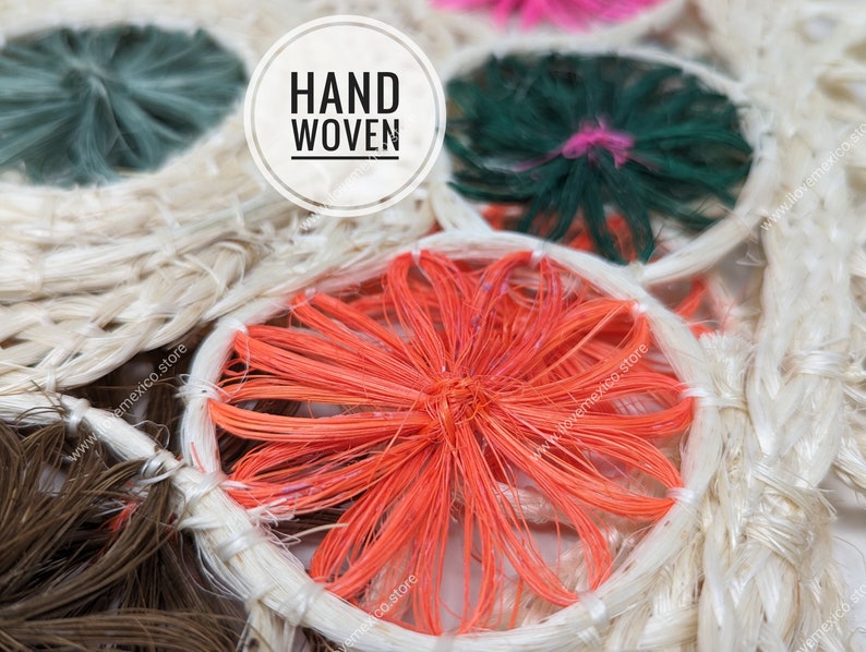 Pu&ograve; includere: Un tessuto intrecciato a mano con motivi circolari a fibre radianti nei toni dell'arancione, verde scuro e marrone, su uno sfondo intrecciato beige naturale. Una sovrapposizione grafica circolare bianca contiene il testo nero HAND WOVEN.