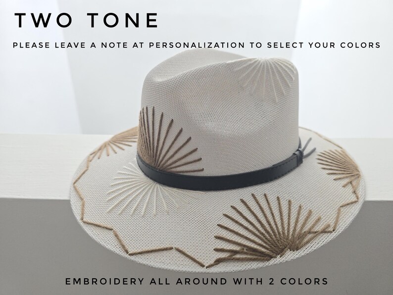 May include: A cream-colored fedora hat featuring a black leather band and sunburst-style embroidery in two shades of brown. The text on the image reads: TWO TONE, PLEASE LEAVE A NOTE AT PERSONALIZATION TO SELECT YOUR COLORS, EMBROIDERY ALL AROUND WITH 2 COLORS.