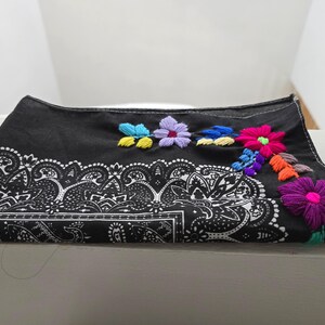 May include: A black bandana featuring a white paisley print along the bottom edge and colorful floral embroidery in shades of pink, purple, blue, yellow, and orange stitched onto the upper right corner of the fabric.