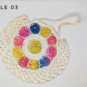 Pu&ograve; includere: Una borsa a rete intrecciata color bianco sporco con il testo STYLE 03 nell'angolo in alto a sinistra. Il centro della borsa &egrave; decorato con un motivo circolare di piccoli elementi floreali dai colori vivaci in rosa, giallo e blu.