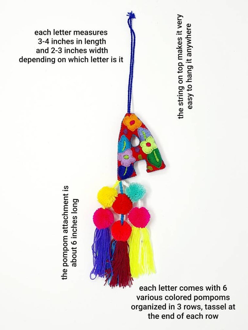 May include: A colourful felt letter A with embroidered flowers, a blue string for hanging, and a tassel of six multi-coloured pompoms. The letter measures 3-4 inches in length and 2-3 inches in width. The pompom attachment is about 6 inches long.