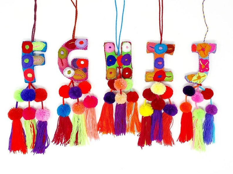 May include: Five colourful felt letter ornaments with pom-pom tassels. The letters are F, G, H, I, and J. Each letter is decorated with colourful embroidery and has a string for hanging.