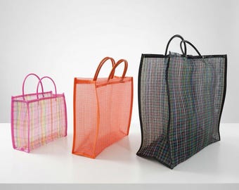 Könnte beinhalten: Drei rechteckige Tragetaschen aus halbtransparentem Netzmaterial. Die kleinste Tasche ist rosa mit Karomuster, die mittlere Tasche ist einfarbig orange und die größte Tasche ist schwarz mit einem mehrfarbigen Gittermuster und schwarzem Rand.