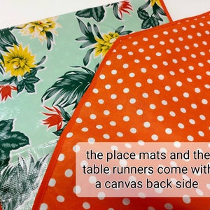 May include: Two placemats and a table runner with a tropical floral print on a light green background. The placemats and table runner have a solid orange back with white polka dots. The text "the place mats and the table runners come with a canvas back side" is printed on the orange fabric.