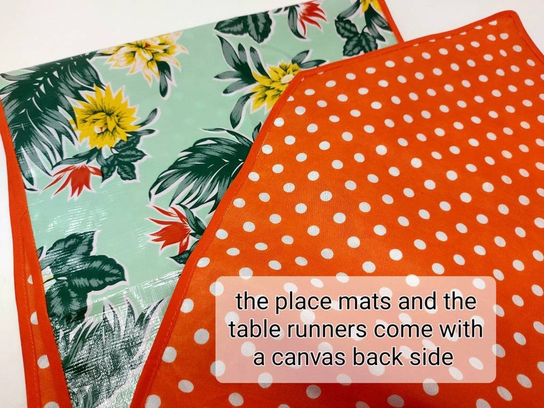 May include: Two placemats and a table runner with a tropical floral print on a light green background. The placemats and table runner have a solid orange back with white polka dots. The text "the place mats and the table runners come with a canvas back side" is printed on the orange fabric.