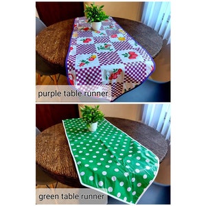 May include: Two table runners, one purple with a checkered pattern and fruit design, and one green with white polka dots. Both runners are on a brown wicker table with a plant in a pot on each runner.