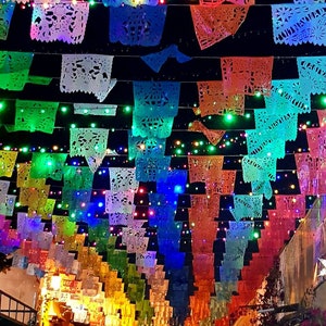 May include: A street decorated with colorful paper lanterns, known as "papel picado", strung across the street. The lanterns are illuminated by twinkling lights, creating a festive atmosphere.