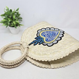 Könnte beinhalten: Eine Strohtasche mit einem blauen und weißen Herzdesign. Die Tasche hat eine runde Form und einen geflochtenen Henkel.