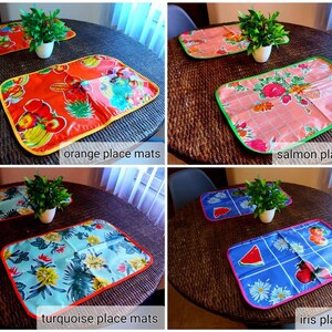 May include: Four placemats with different designs and colors. The placemats are on a woven surface. The placemats are labeled "orange place mats", "salmon place mats", "turquoise place mats", and "iris place mats".