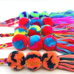 Puede incluir: Una colección de pompones coloridos con borlas de hilo multicolor y cordones trenzados estilo pulsera de la amistad. Los pompones presentan una mezcla de colores brillantes como rojo, azul, verde y naranja, creando un diseño lúdico y llamativo.