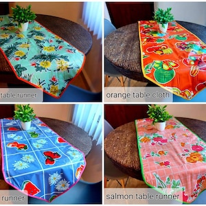 May include: Four table runners in different colors and patterns. The table runners are turquoise with tropical leaves and flowers, orange with fruit, blue with watermelons and daisies, and salmon with pink roses and green leaves.  The table runners are all on a brown wicker table.