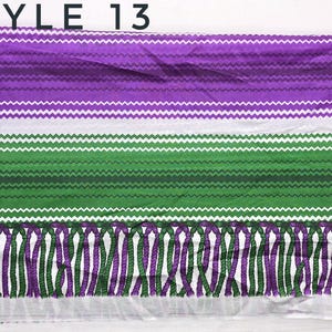 May include: A rectangular textile featuring the text STYLE 13 at the top. The fabric displays horizontal bands of purple and green, each decorated with a white zigzag pattern. The bottom edge is finished with a fringe of alternating purple and green.