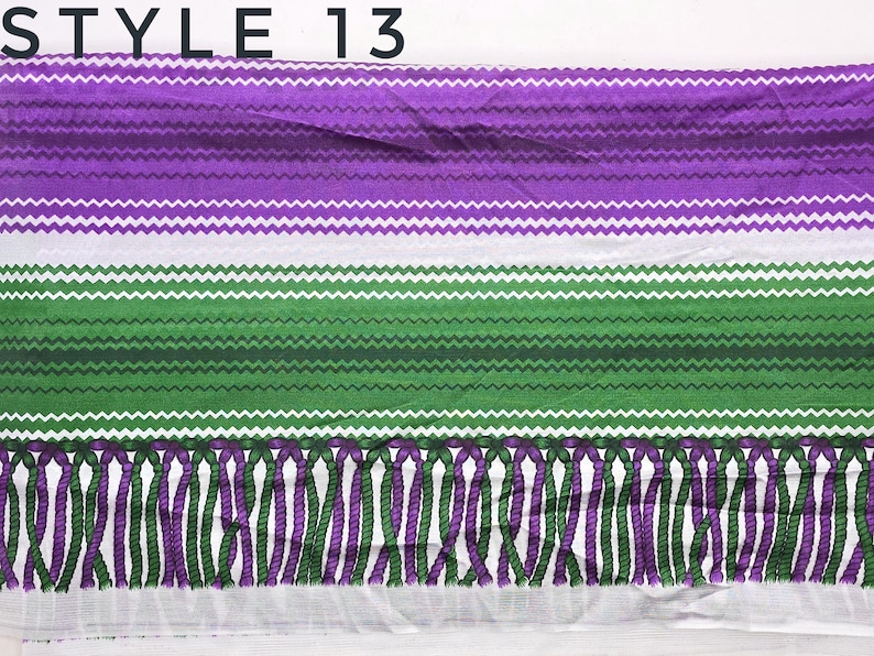 May include: A rectangular textile featuring the text STYLE 13 at the top. The fabric displays horizontal bands of purple and green, each decorated with a white zigzag pattern. The bottom edge is finished with a fringe of alternating purple and green.