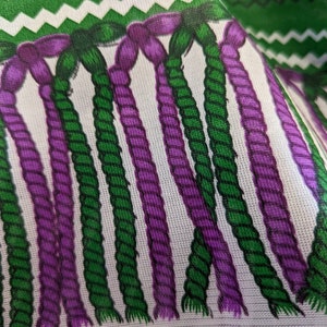 May include: A fabric featuring a repeating pattern of vertical, twisted rope-like strands in alternating shades of deep purple and forest green against a white background, topped with a horizontal band of green and white zigzag chevron stripes.