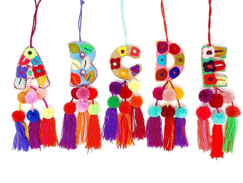 May include: Five colourful felt letter ornaments with embroidered flowers and pom-poms. The letters are A, B, C, D, and E.