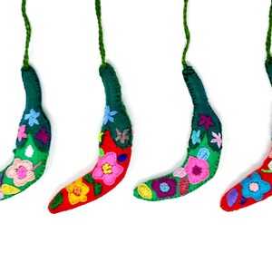 May include: Four handmade felt banana decorations with colourful embroidered flowers. Each ornament has a green stem and a red body with a variety of flower designs.