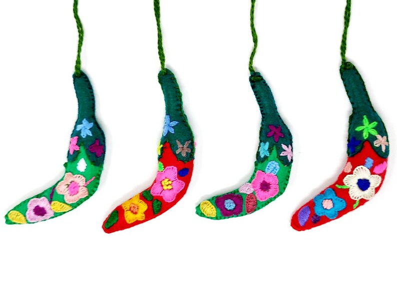 May include: Four handmade felt banana decorations with colourful embroidered flowers. Each ornament has a green stem and a red body with a variety of flower designs.