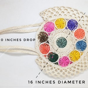 Pu&ograve; includere: Una borsa tote rotonda in tessuto color crema con un motivo circolare centrale circondato da colorati accenti di filato a forma di stella in rosa, giallo, viola, arancione, blu, verde e marrone. Ha un manico di 25,4 cm e un diametro di 40,6 cm.