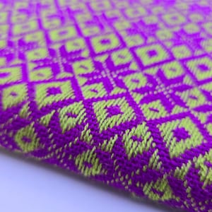 May include: A woven textile fabric featuring a vibrant geometric pattern in bright purple and lime green. The design consists of repeating diamond and square shapes created by the interlacing threads, showing a textured surface with a visible weave.