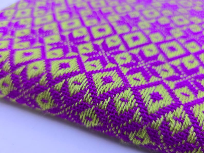 May include: A woven textile fabric featuring a vibrant geometric pattern in bright purple and lime green. The design consists of repeating diamond and square shapes created by the interlacing threads, showing a textured surface with a visible weave.