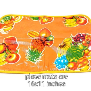 May include: Orange place mat with a yellow border and a colorful fruit design. The place mat is 16x11 inches.