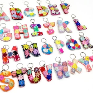 May include: A set of 26 colourful felt letter keychains, each letter is embroidered with colourful flowers. The keychains are arranged in alphabetical order.