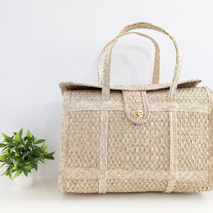 May include: A woven straw tote bag with a brown leather handle and a gold metal clasp. The bag has a rectangular shape and is made of a natural, light brown material.