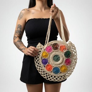 Pu&ograve; includere: Una borsa tote rotonda in tessuto beige con un motivo circolare centrale circondato da cerchi pi&ugrave; piccoli con motivi a stella in tonalit&agrave; rosa, arancione, giallo, viola, blu, verde e marrone, dotata di due lunghi manici a spalla.