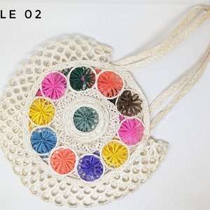 Pu&ograve; includere: Una borsa rotonda intrecciata color bianco sporco con due lunghi manici, che riporta il testo STYLE 02 nell'angolo in alto a sinistra. La borsa presenta un motivo circolare centrale circondato da dieci piccoli accenti intrecciati a forma di stella nei colori rosa, verde, arancione, marrone, giallo, blu e viola.